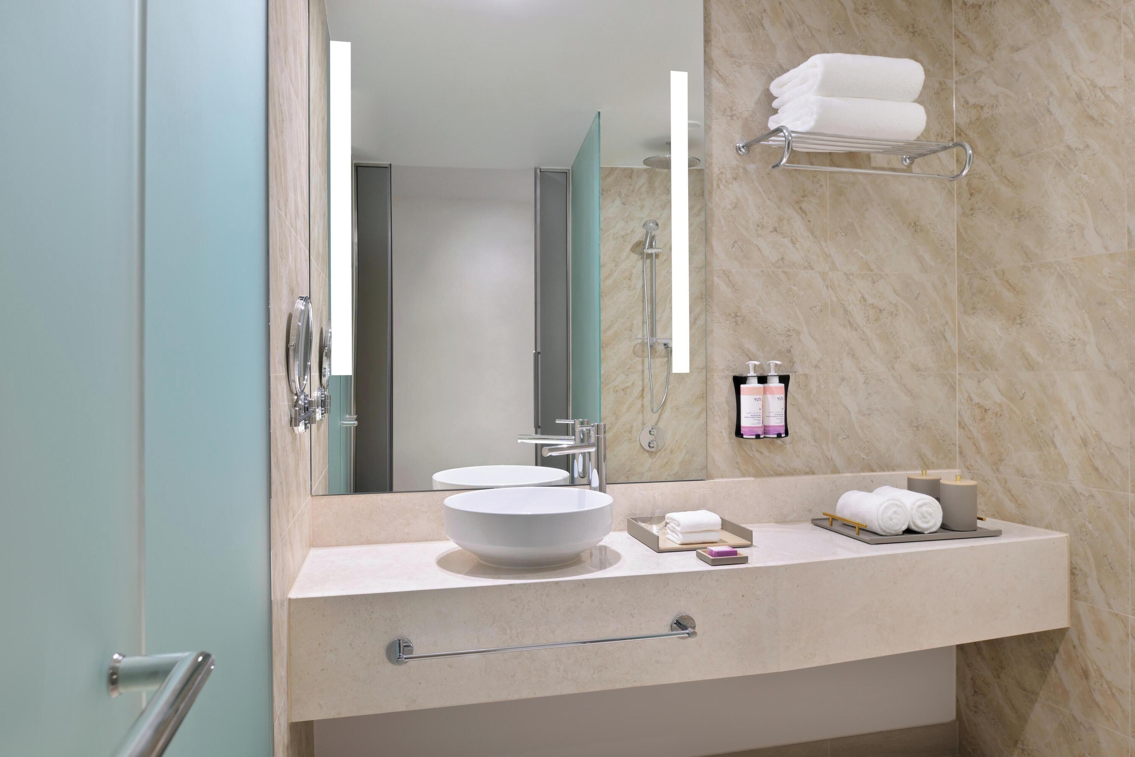 Un baño moderno con un espejo grande, dos lavamanos, un perchero para toallas y un mueble de tocador con dispensador de toallas.