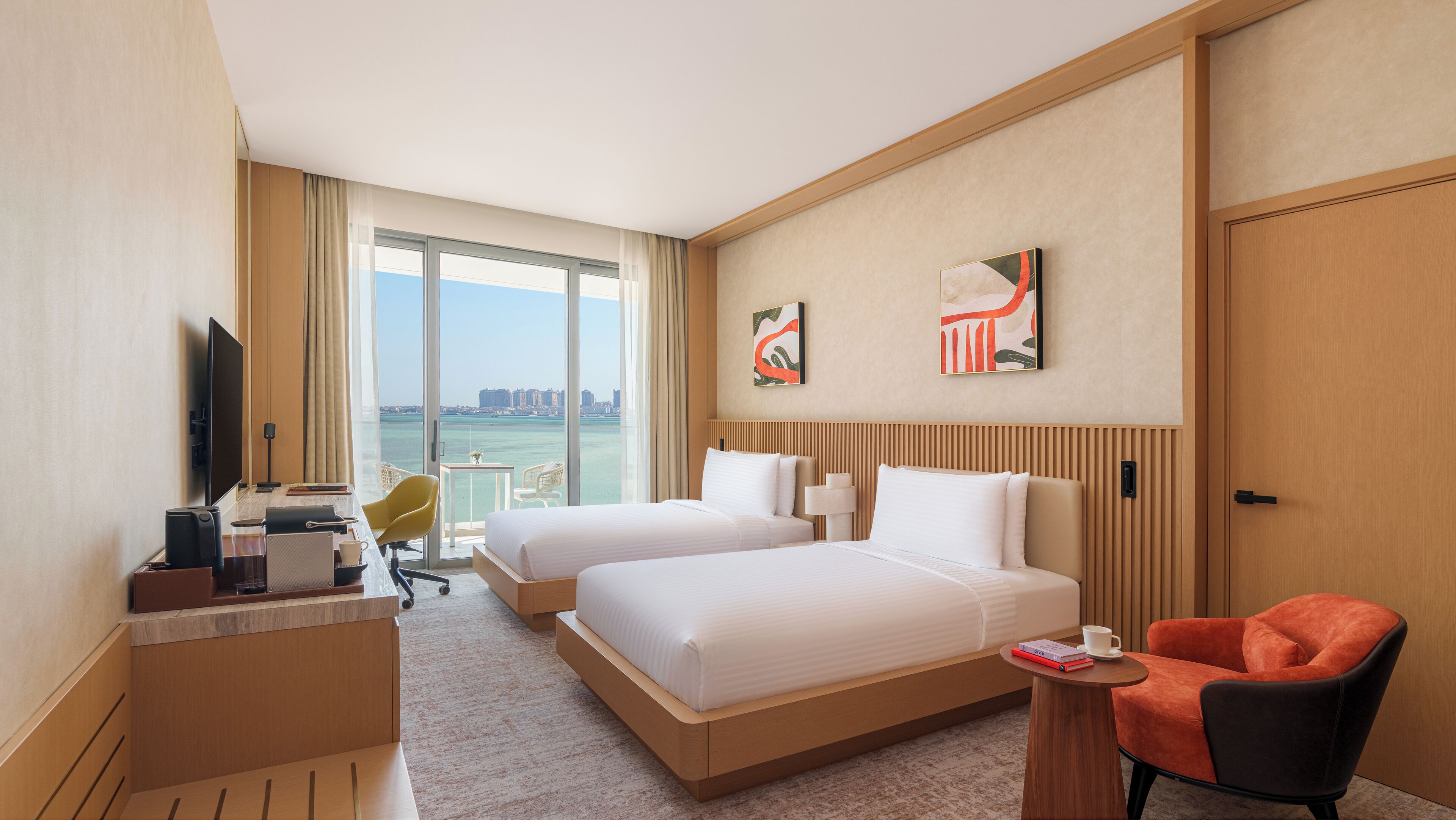 A hotel room with two beds, a desk with a computer, a chair, and a view of the city.