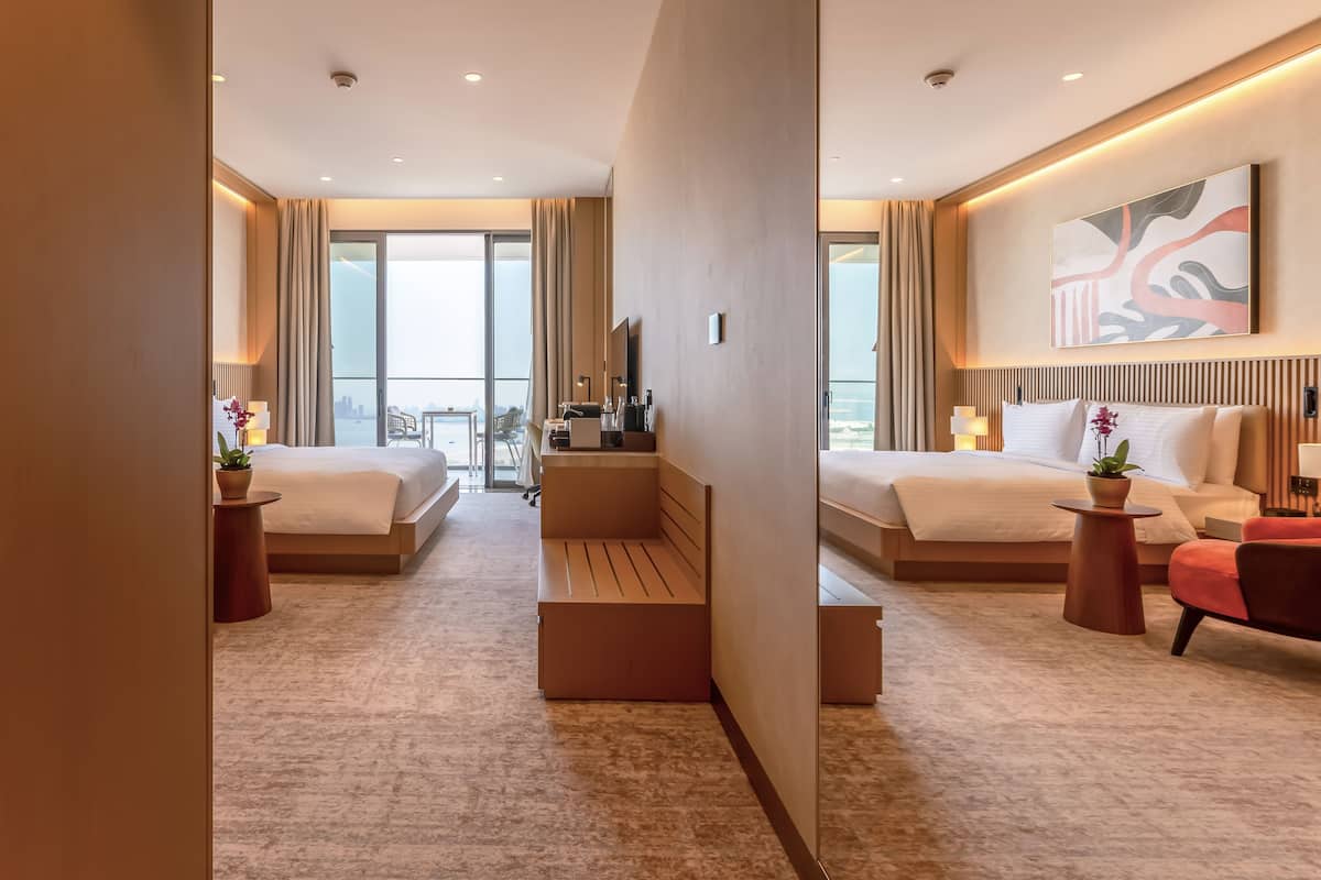 Une chambre d’hôtel moderne avec deux lits, un balcon offrant une vue sur la ville et un coin repas avec une table et des chaises.