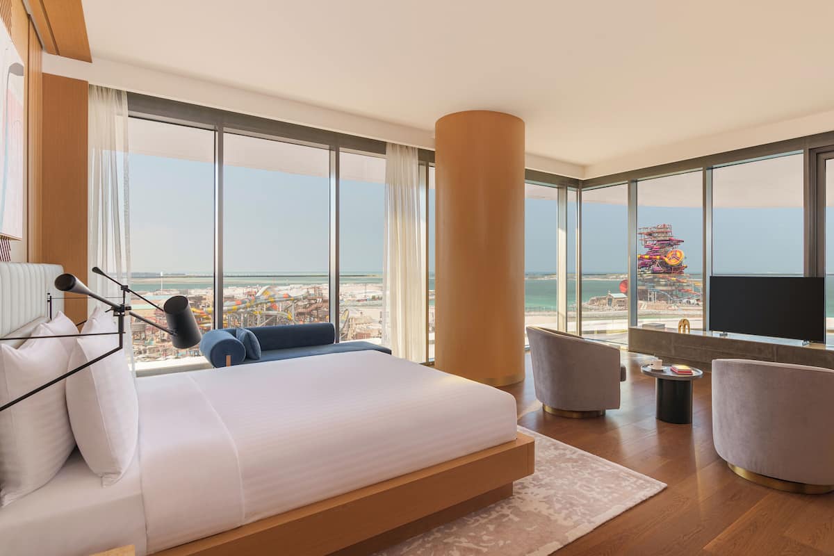 Une chambre d’hôtel moderne dotée d’un grand lit, d’une télévision et d’un balcon offrant une vue sur la plage et le parc d’attractions.
