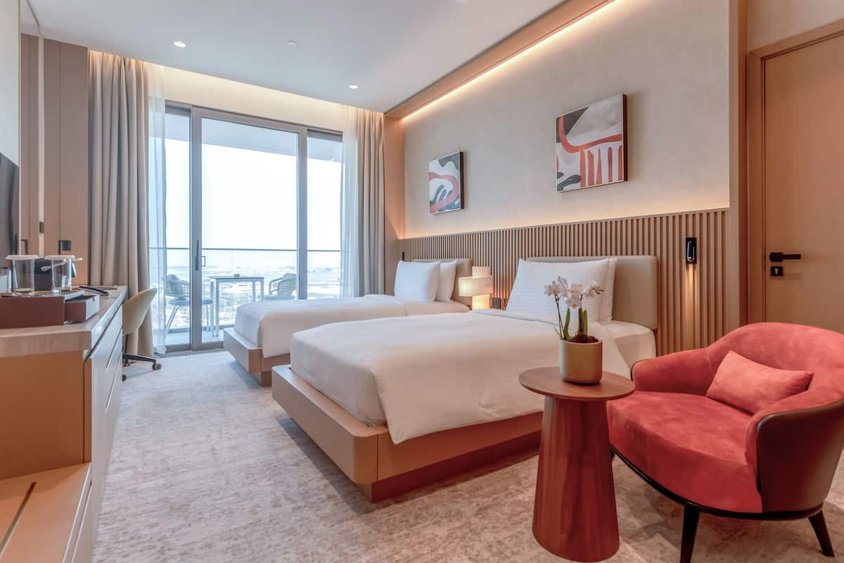 Une chambre d’hôtel avec deux lits, un bureau, une chaise et une vue sur la ville.