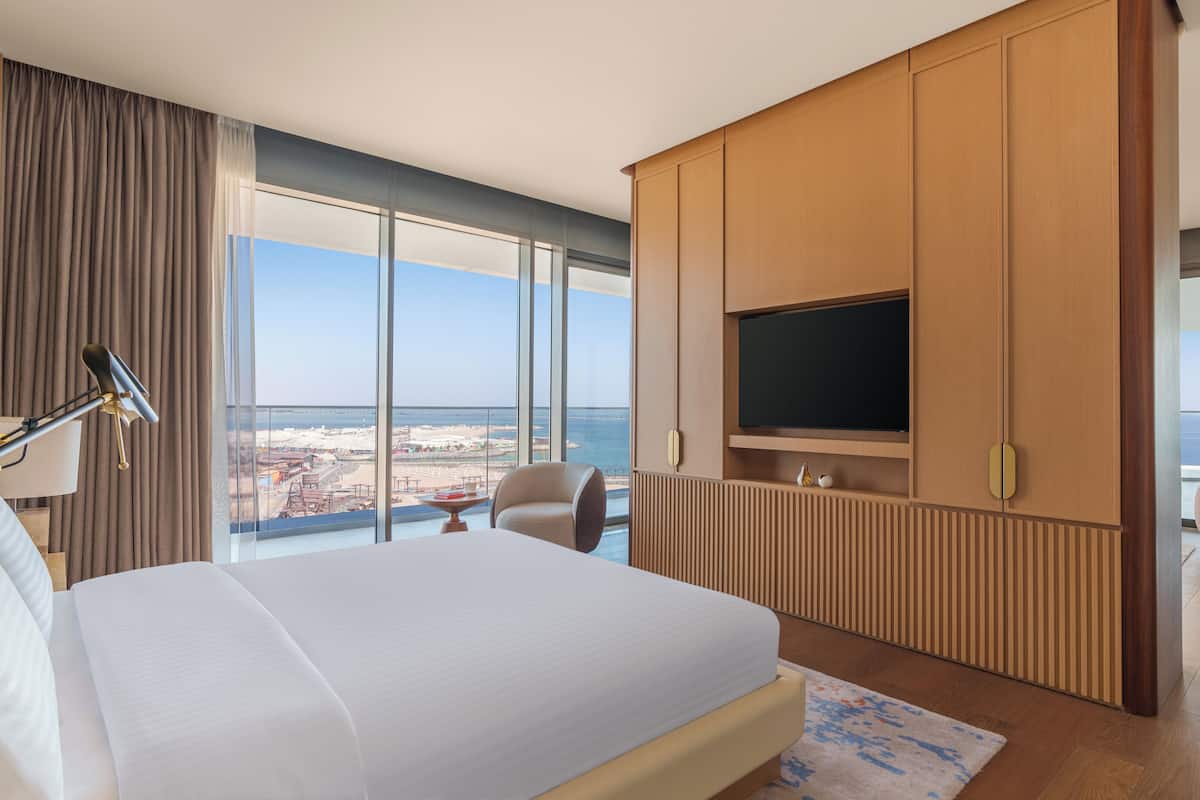 Une chambre d’hôtel avec un grand lit, un téléviseur fixé au mur et une vue sur la mer.