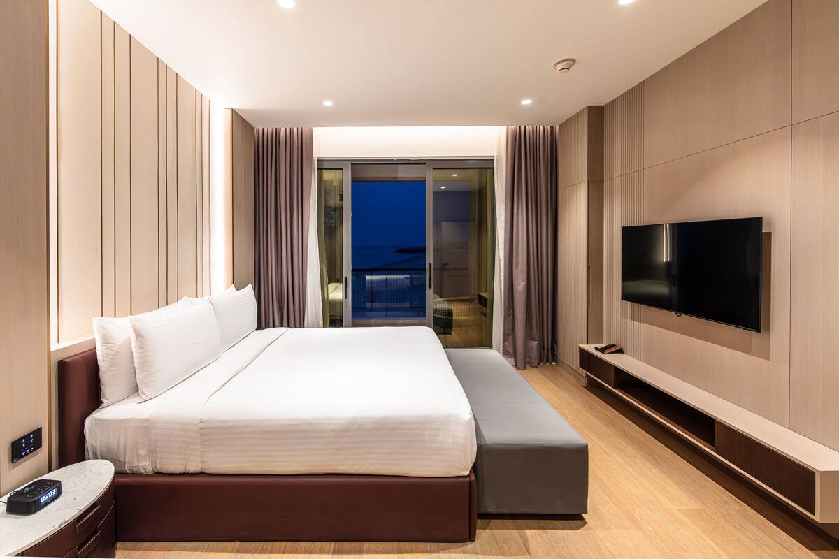 Une chambre d’hôtel moderne dotée d’un grand lit, d’une télévision à écran plat, d’une table de chevet et offrant une vue sur le balcon.