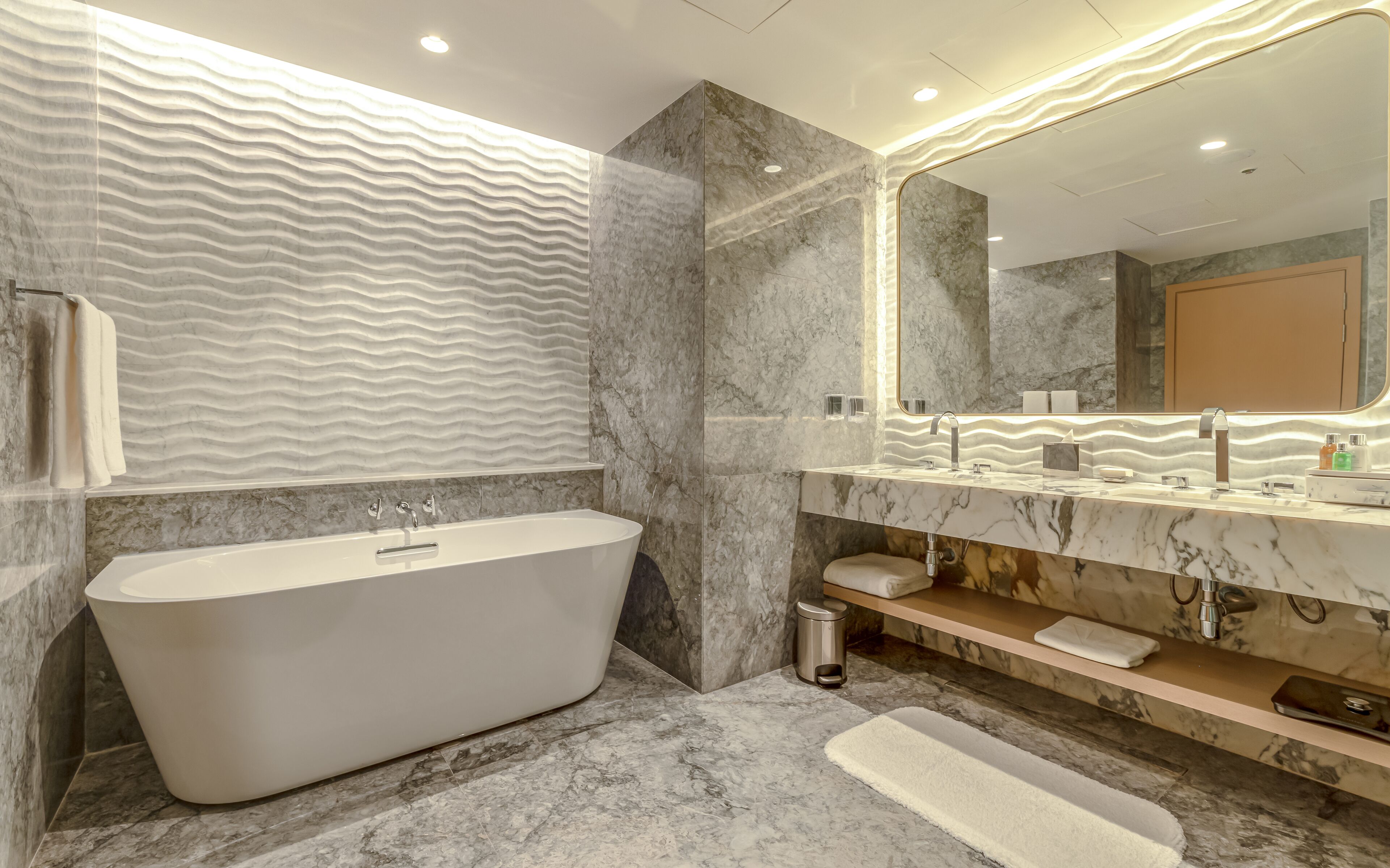 Un baño moderno con una bañera independiente, un espejo grande y paredes de mármol.
