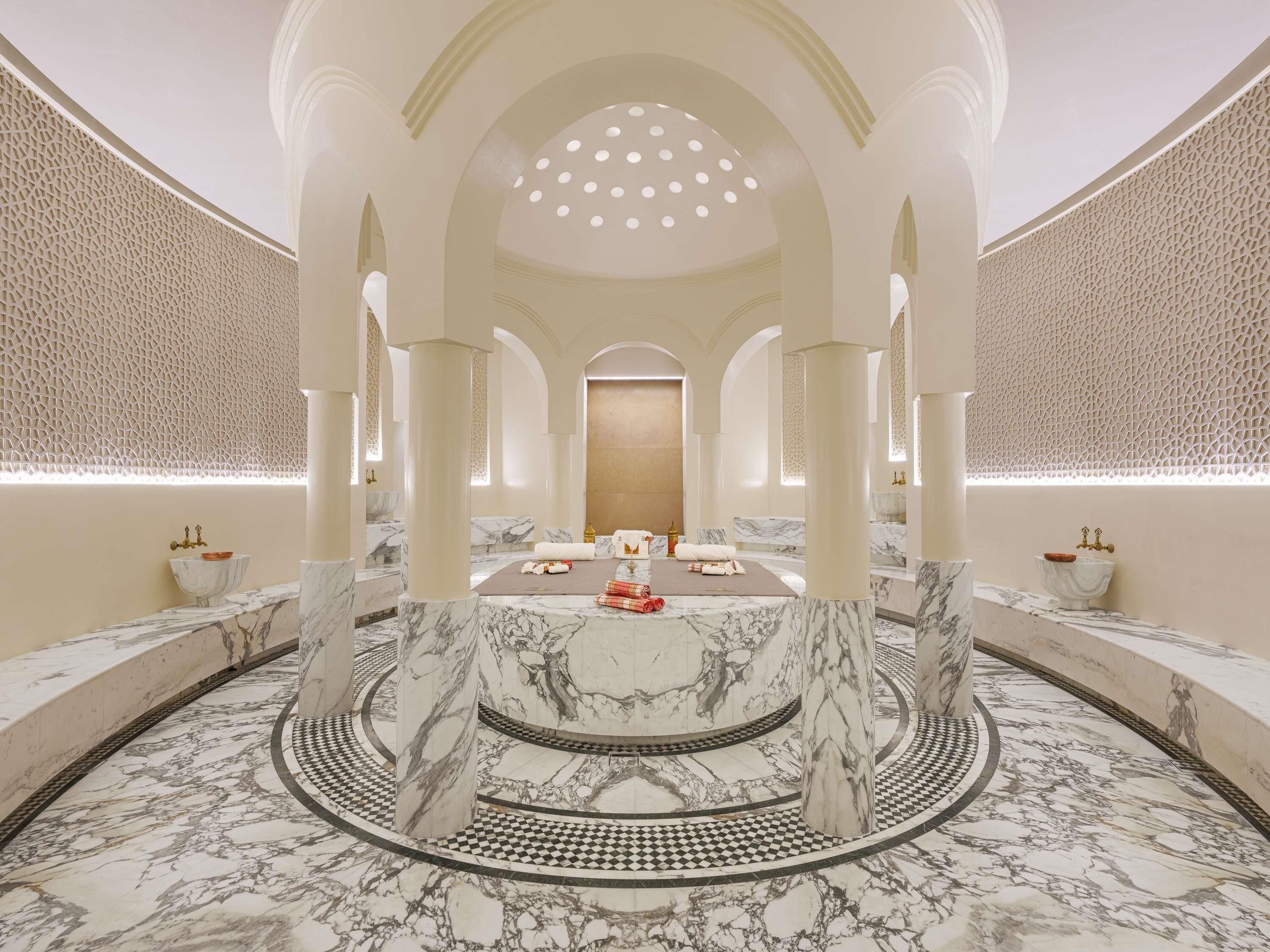 Un baño lujoso con suelo de mármol, una zona de estar circular central y un techo decorativo.