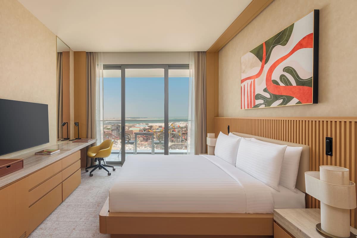 Une chambre d’hôtel dotée d’un grand lit, d’un bureau avec un téléviseur à écran plat, d’une chaise et offrant une vue sur la ville grâce à de grandes fenêtres.