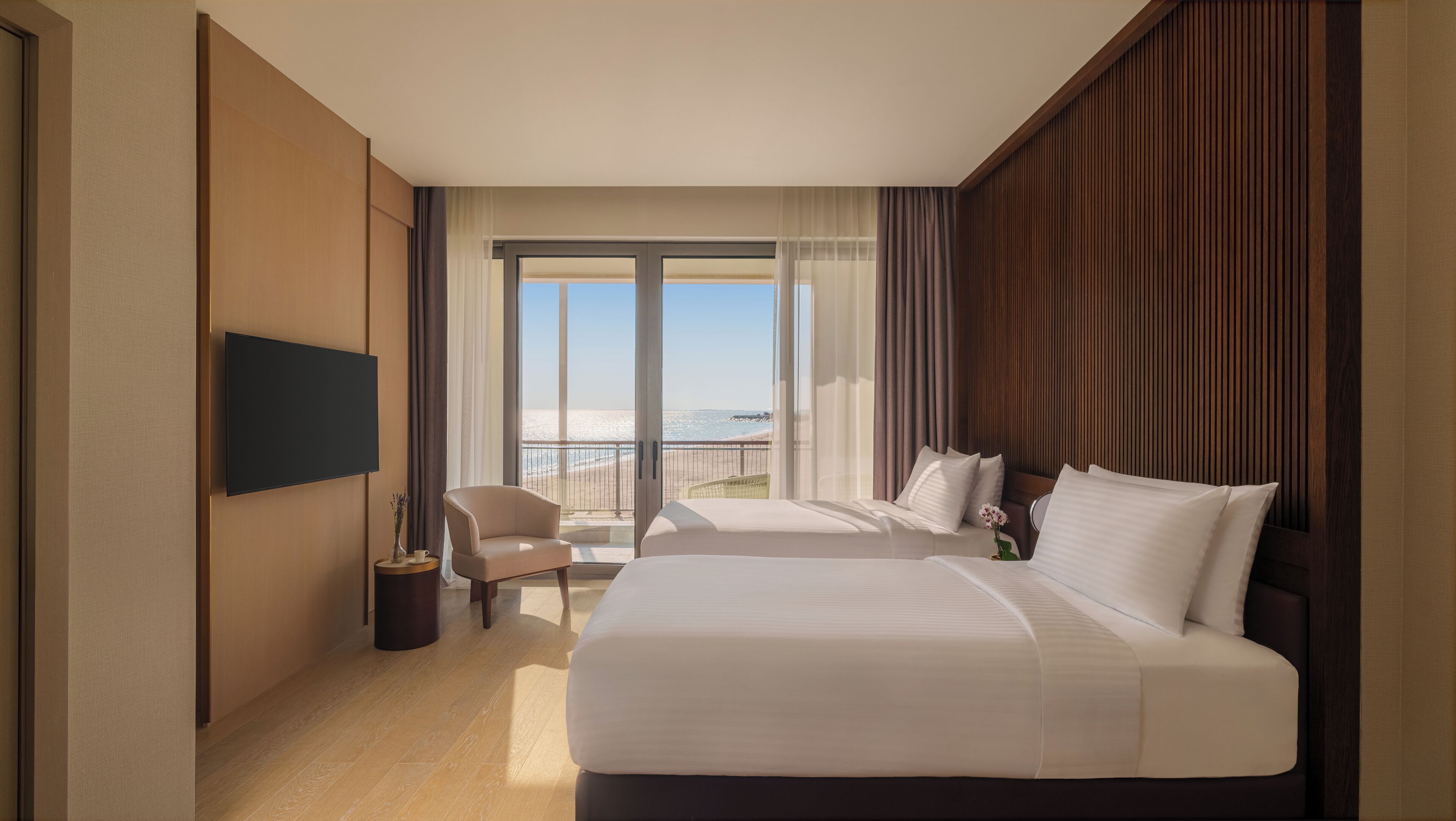 Une chambre d’hôtel avec deux lits, une télévision, une chaise et un balcon donnant sur la plage.