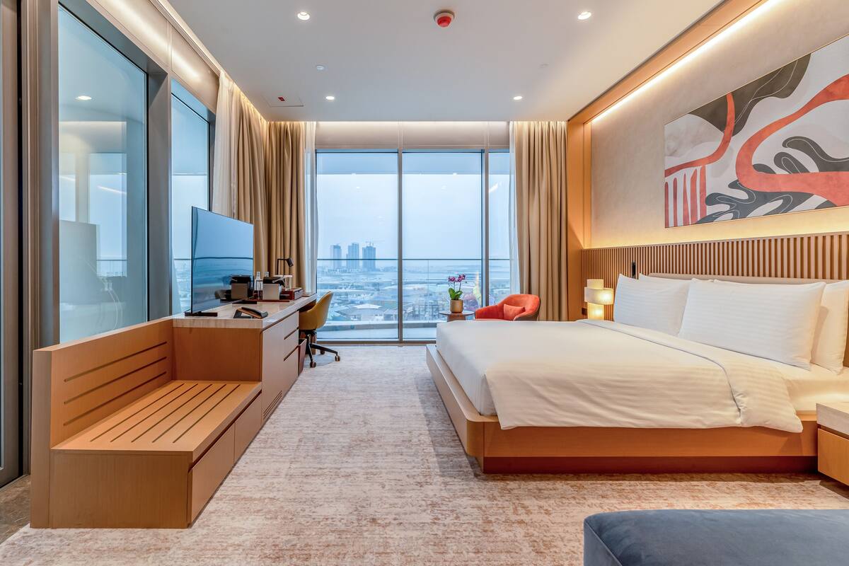 Une chambre d’hôtel moderne dotée d’un grand lit, d’un bureau avec un ordinateur, d’une vue sur la ville et d’une grande fenêtre.