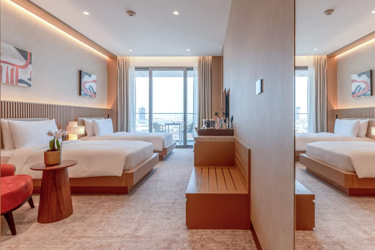 Une chambre d’hôtel avec deux lits, un petit coin salon, un bureau et une vue sur la ville.