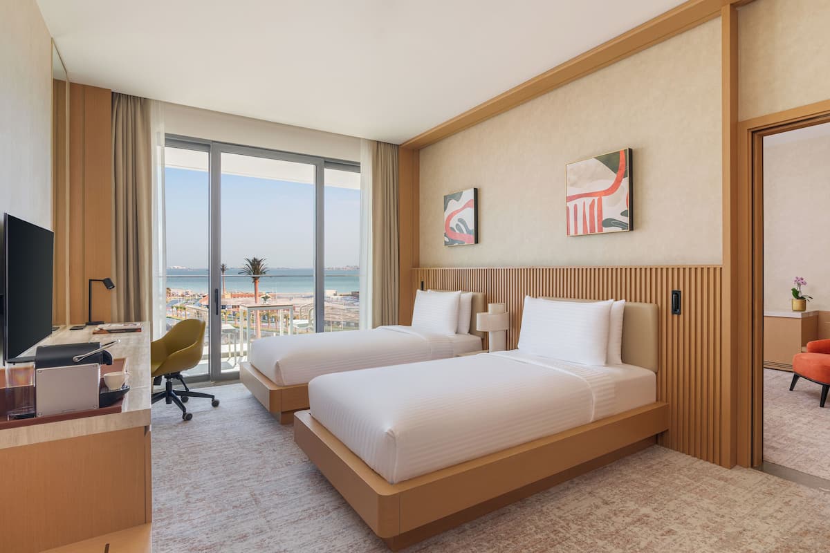 Une chambre d’hôtel avec deux lits, un bureau, une chaise et une vue sur la mer.