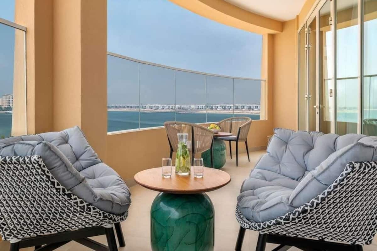 A balcony with two chairs, a table, and a view of the sea.