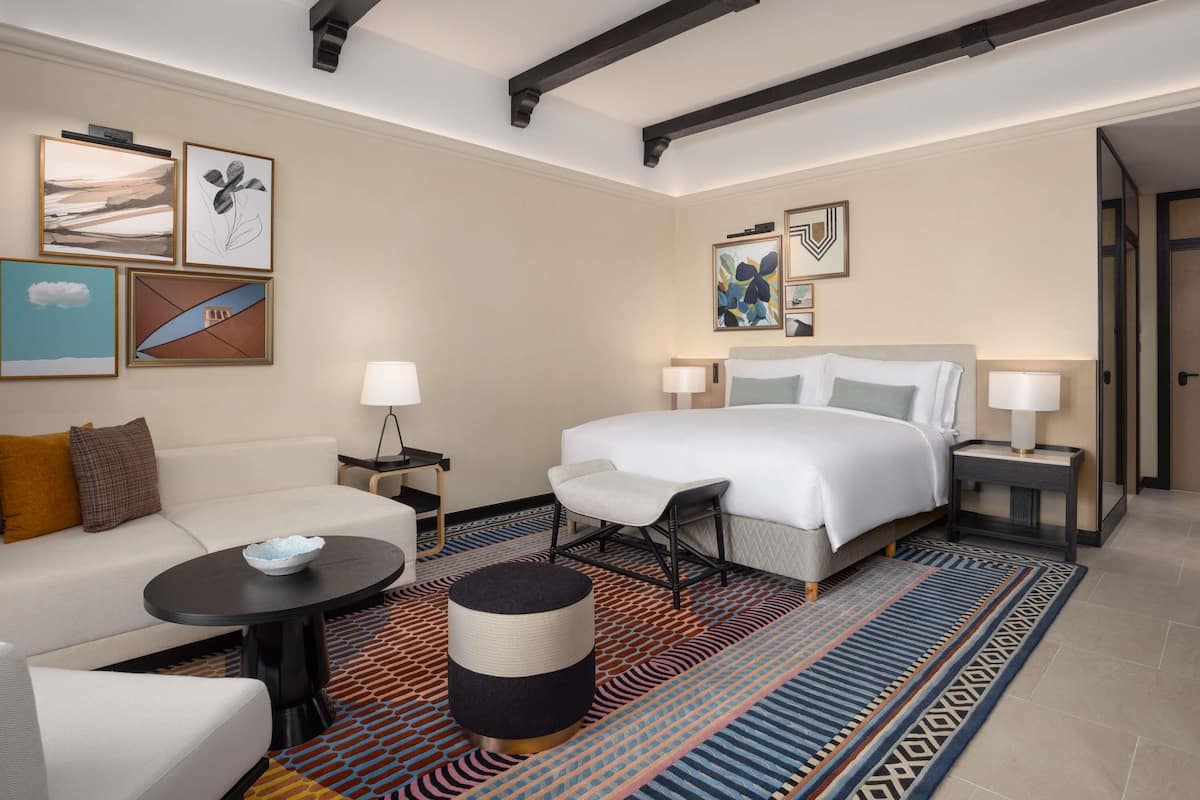 Een hotelkamer met een bed, een bank, een kleine tafel, een lamp en een vloerkleed.