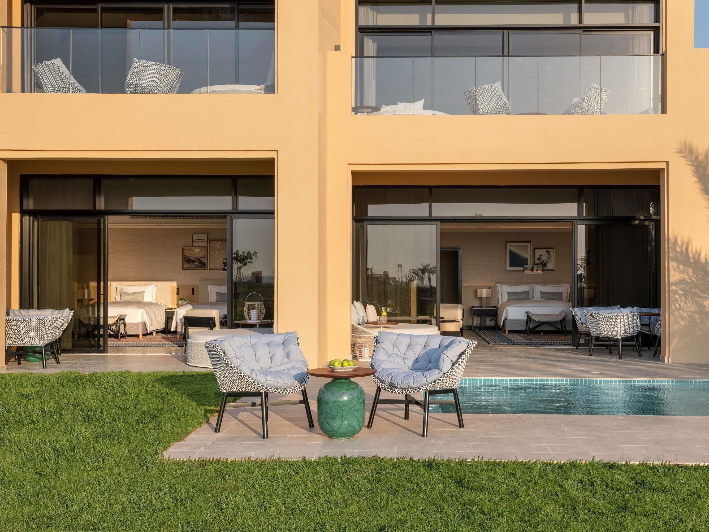 A modern two-story building with a swimming pool, outdoor seating, and a well-maintained lawn.