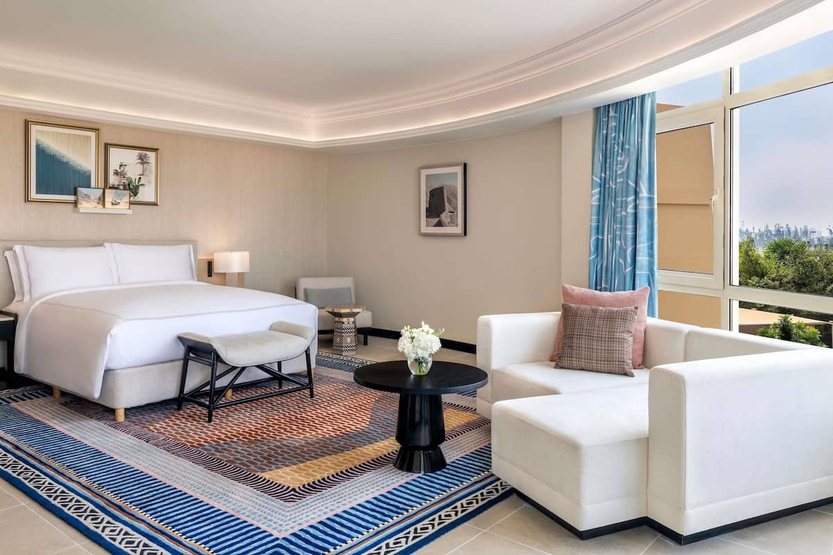 Een hotelkamer met een bed, een stoel, een bank, een klein tafeltje en uitzicht op het omliggende landschap.