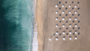 Privat strand, hvit sand, parasoller og strandhåndklær