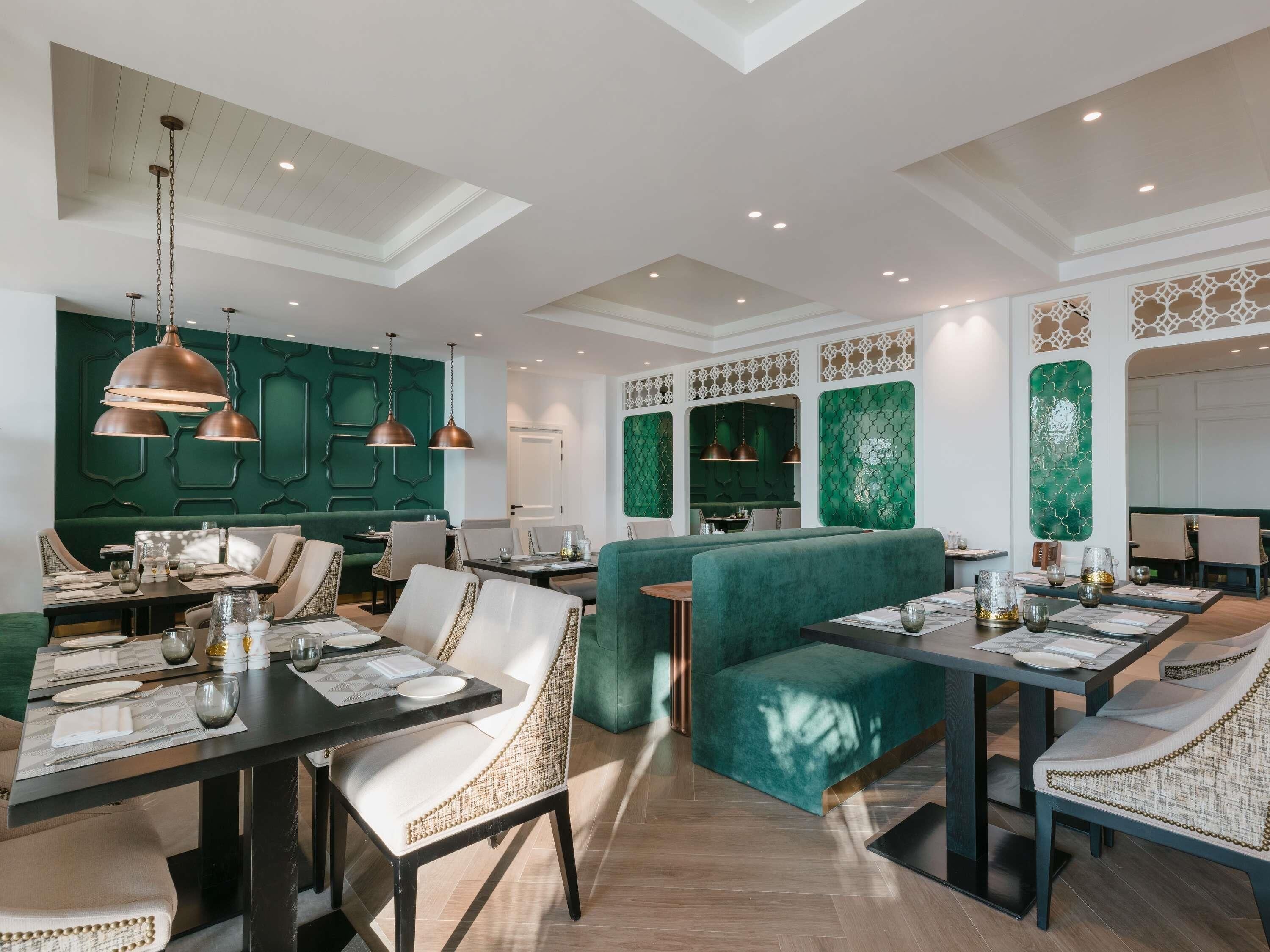 A modern dining area with green upholstered booths, pendant lighting, and a high ceiling with recessed lighting.
