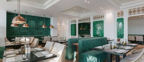 A modern dining area with green upholstered booths, pendant lighting, and a high ceiling with recessed lighting.