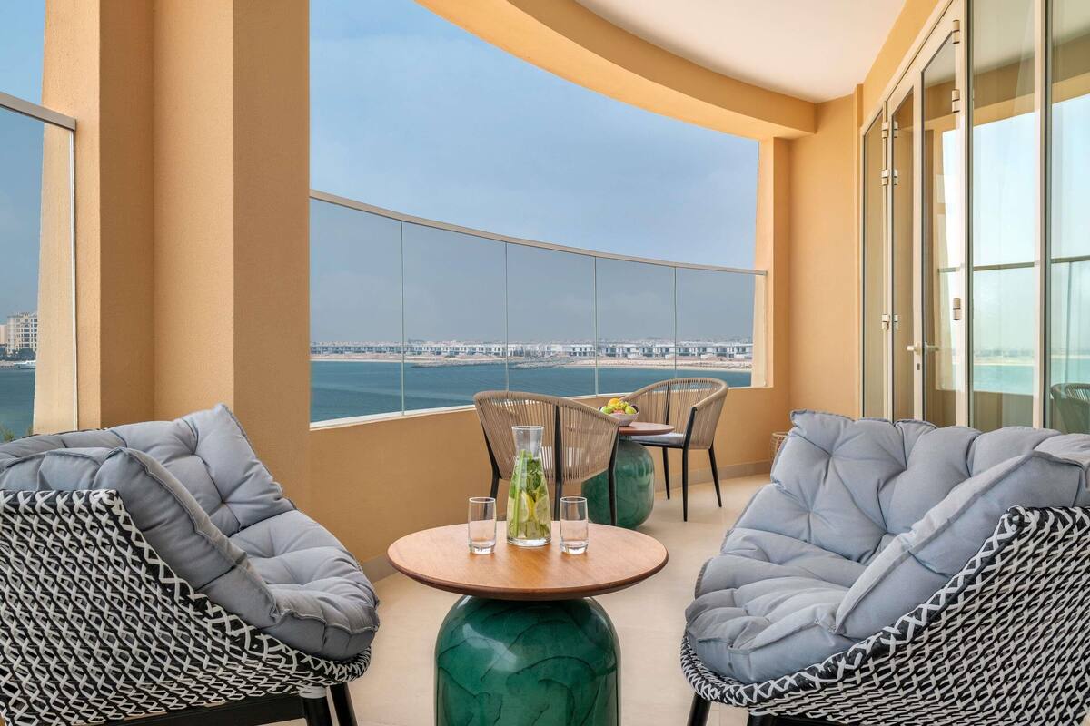 Een balkon met twee stoelen, een tafel en uitzicht op een brug en water.