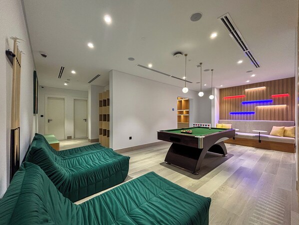 A modern room with a pool table, green sofas, and a seating area with a sofa and a small table. - Sofitel Ras Al Khaimah Al Hamra Beach Resort (Ras Al Khaimah)