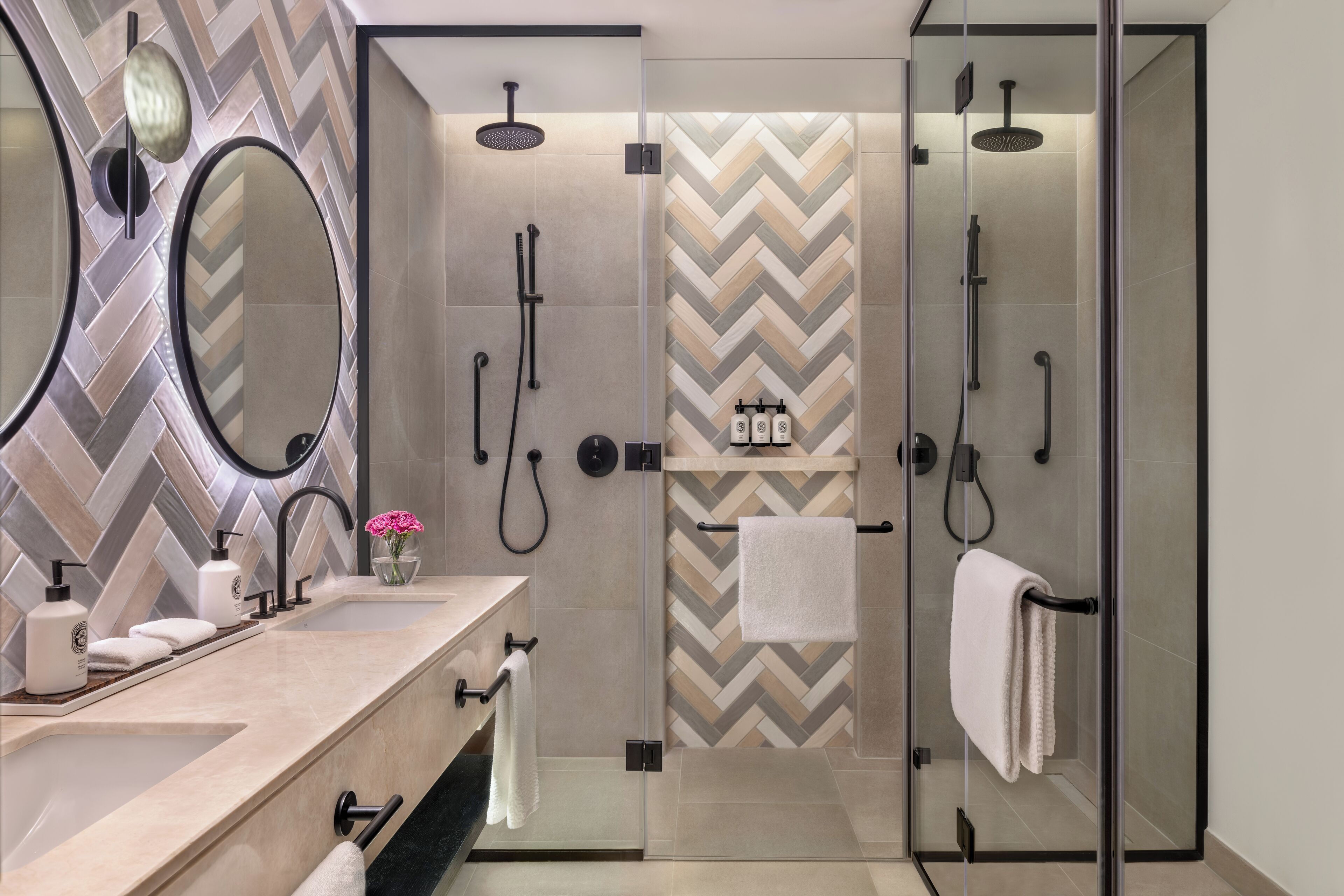 A modern bathroom with a herringbone tile backsplash, a large mirror, a glass-enclosed shower, and a vanity with a sink and towel rack.