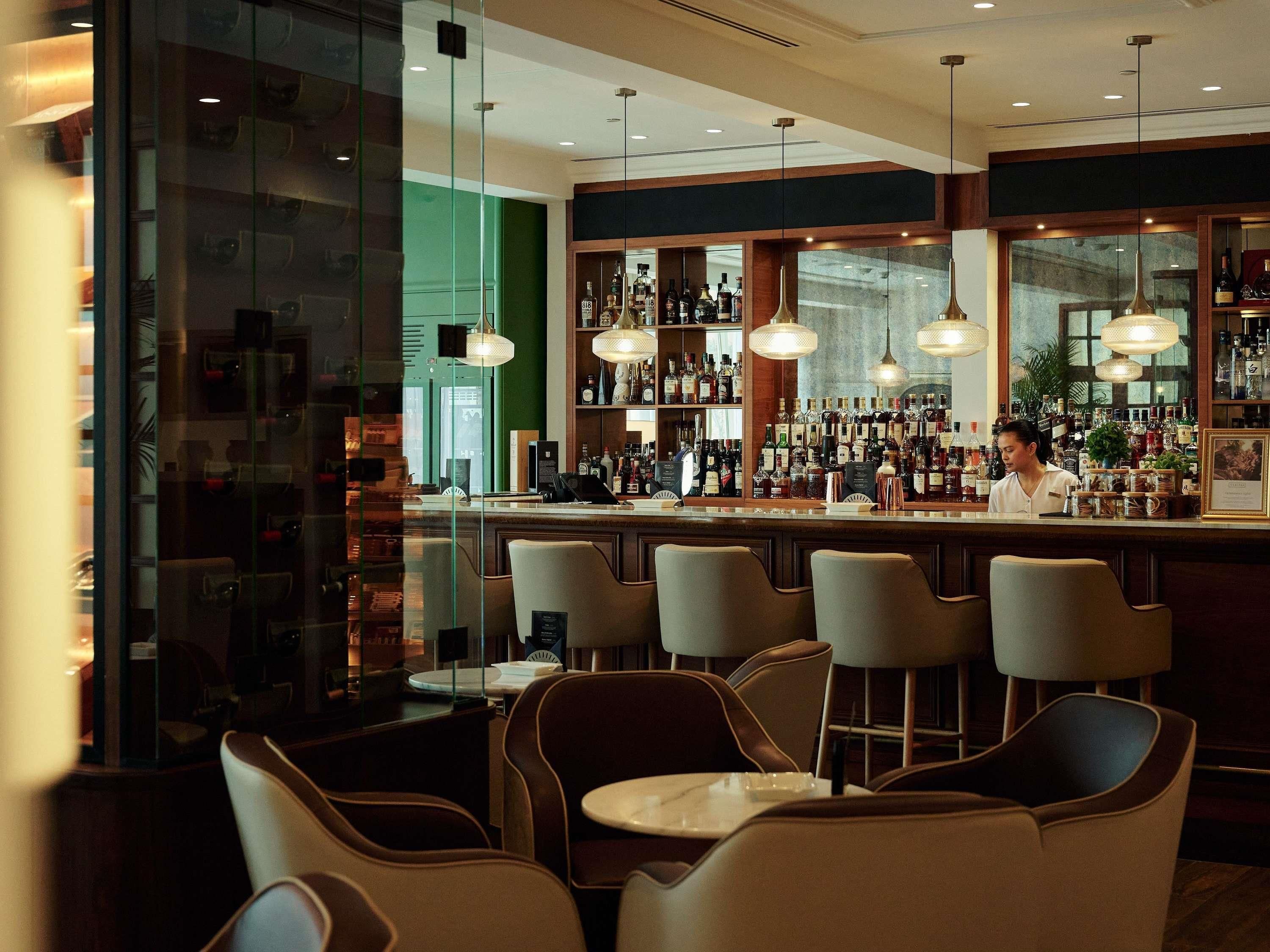 A bar area with a bartender, bar stools, and a variety of bottles.