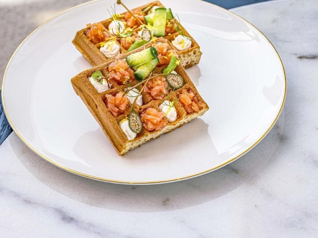 Two square sandwiches on a white plate with a gold rim.