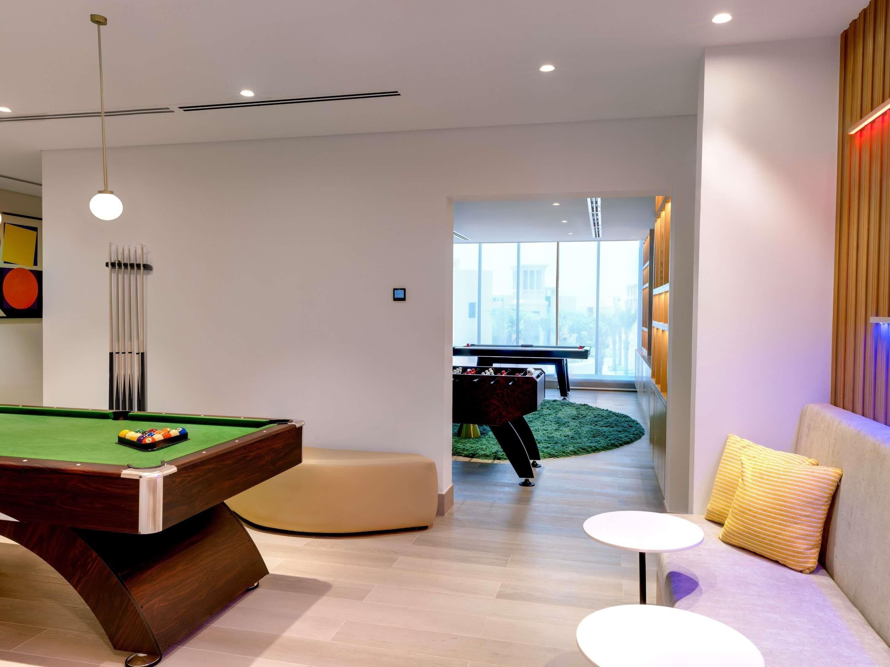 A modern room with a pool table, a snooker table, and a sofa with cushions.