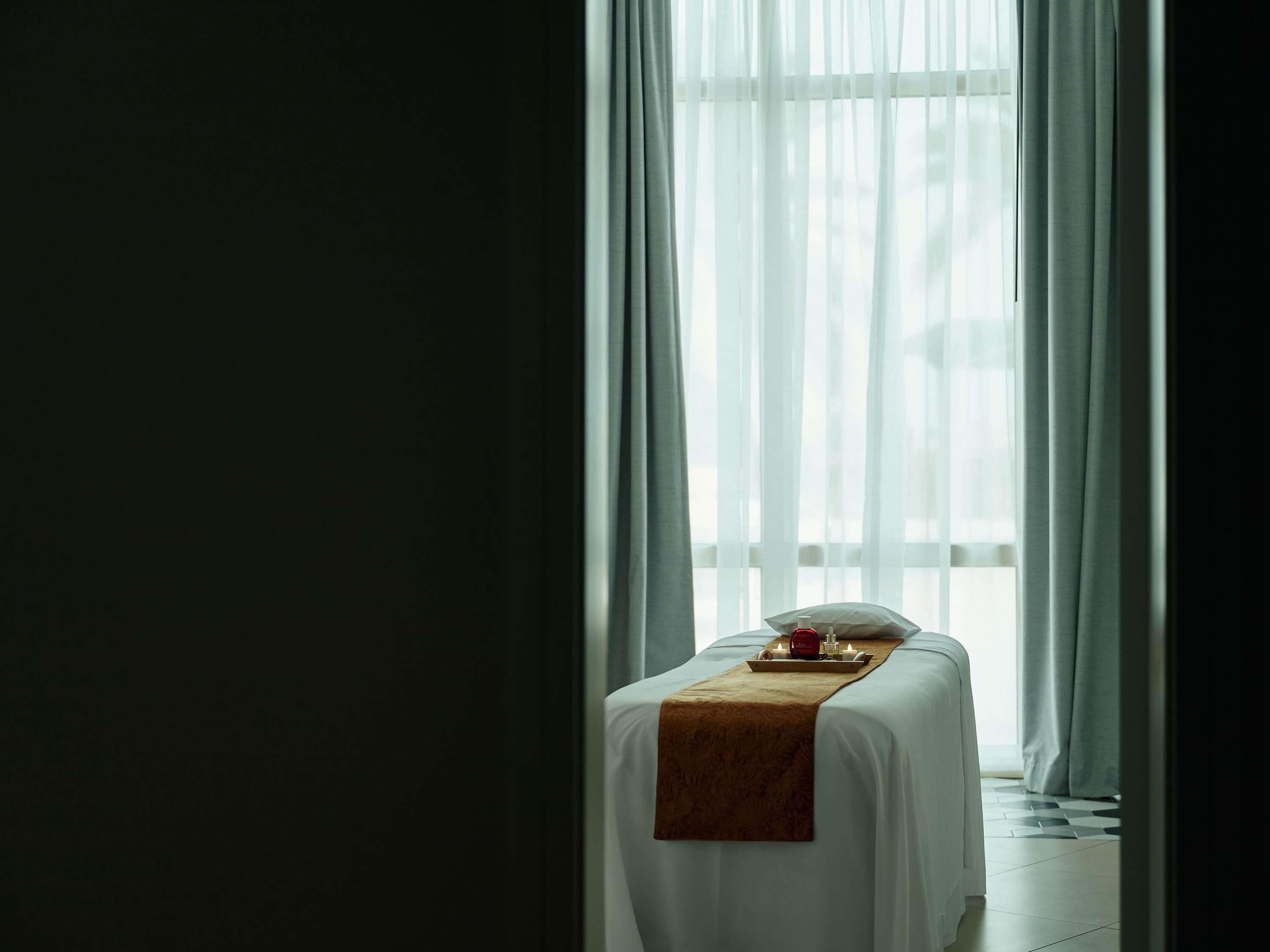 A hotel room with a bed, a tray with candles, and sheer curtains.