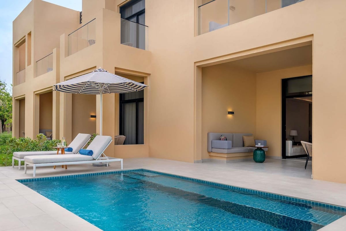 Un edificio moderno con piscina, sillas de descanso y una pequeña zona de estar.