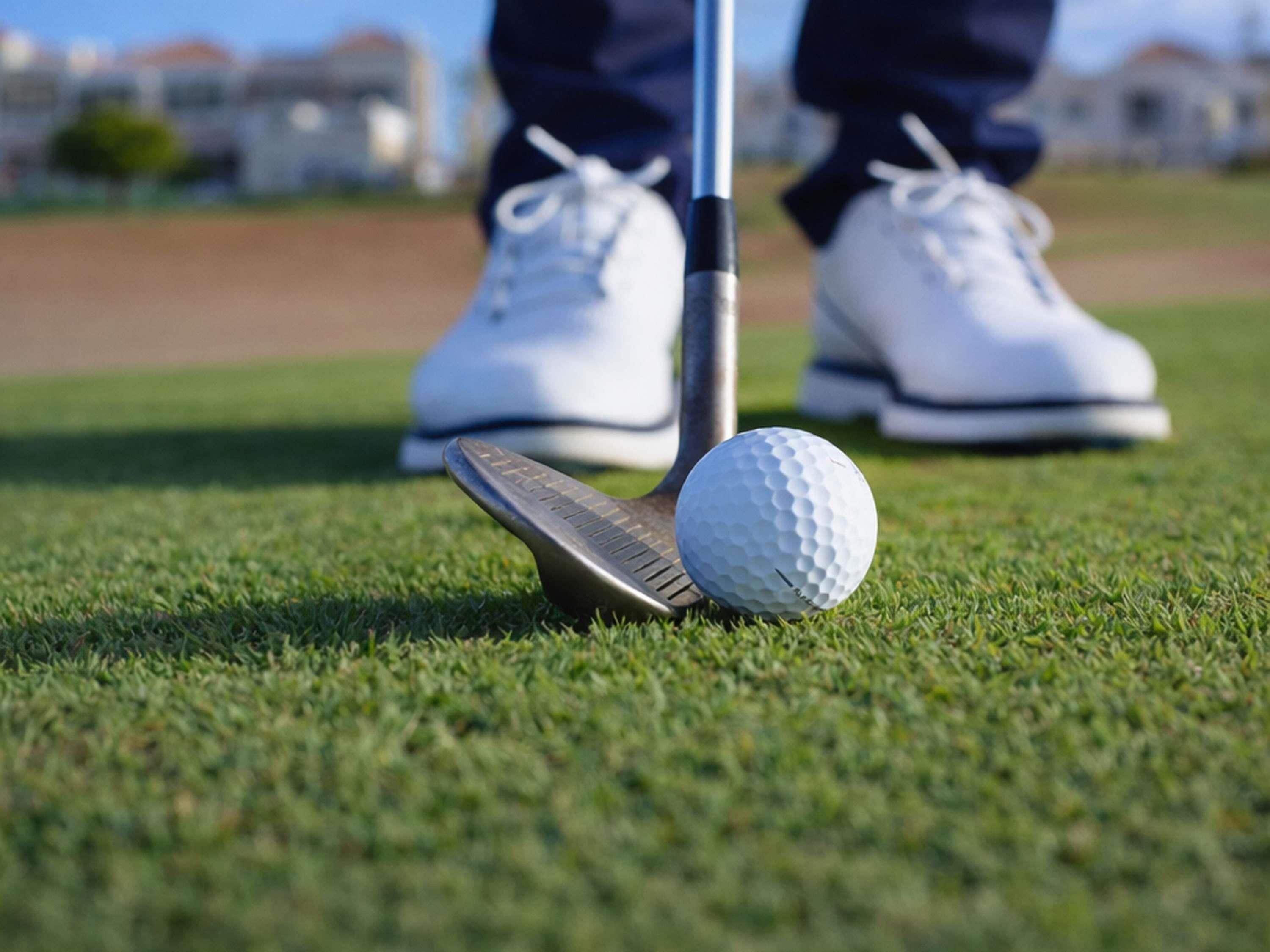 A golf ball on a tee with a golf club behind it, set on a green field.