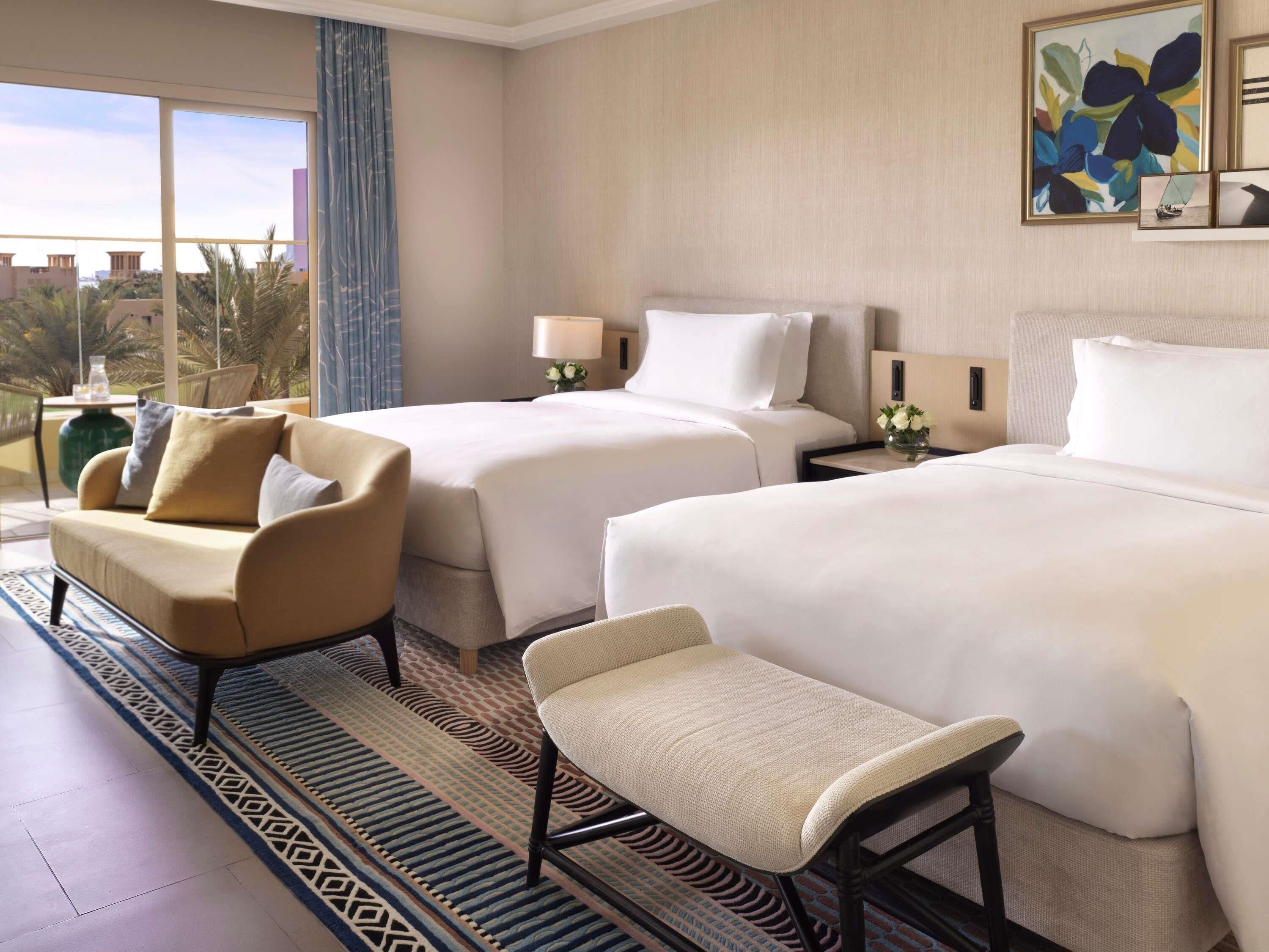 A hotel room with two beds, a sofa, a chair, a window with a view, and a painting on the wall.