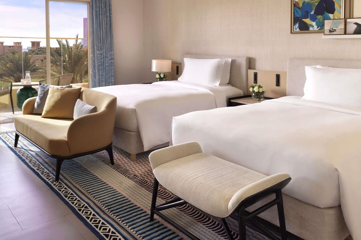 A hotel room with two beds, a sofa, a chair, a window with a view, and a painting on the wall.