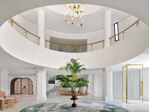 Een meerlaags interieur met een centrale trap, potplanten en een kroonluchter.