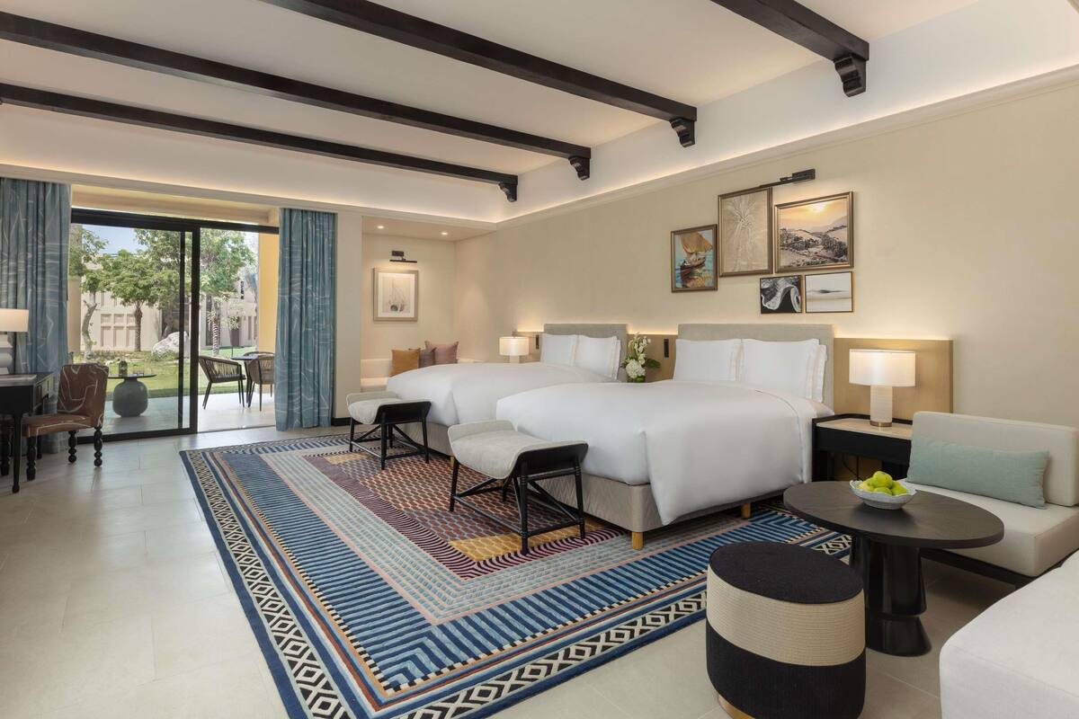 Hotelkamer met een groot bed, twee nachtkastjes, een bank, een eettafel en uitzicht door een schuifdeur op een buitenruimte.