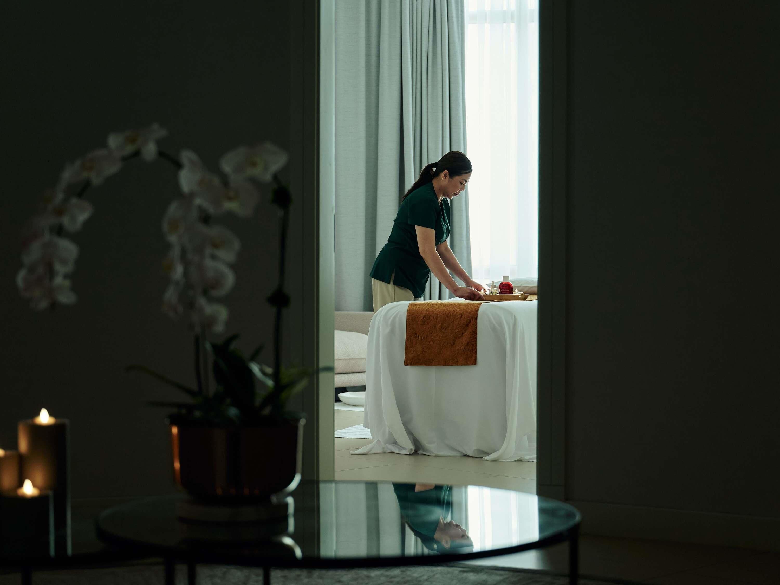 Una habitación con cama, una mesa con bandeja, una planta en maceta y una vela.