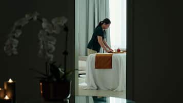Una habitación con cama, una mesa con bandeja, una planta en maceta y una vela.