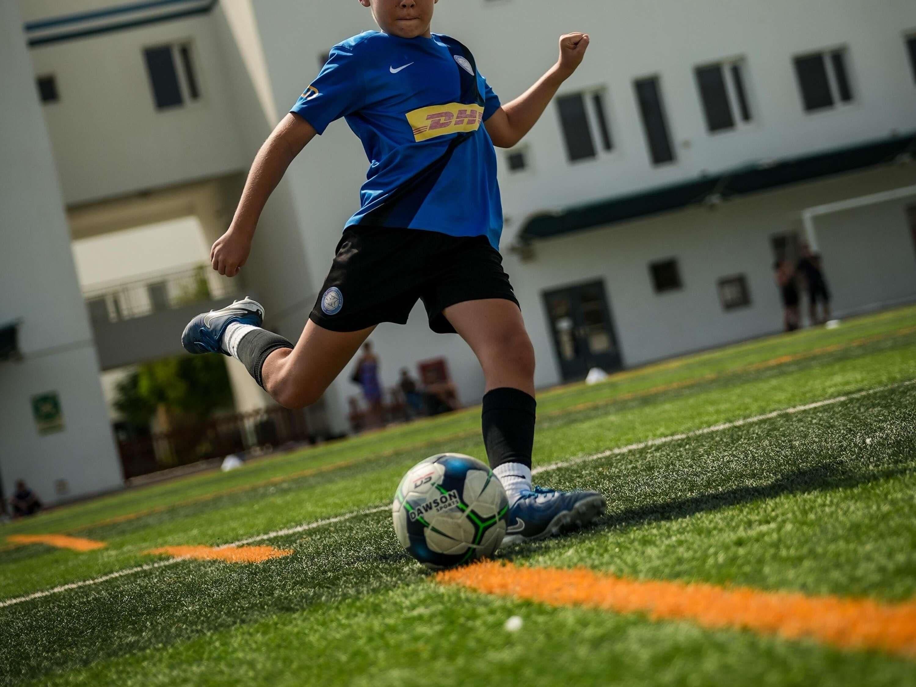 A person playing soccer on a field with a building in the background.