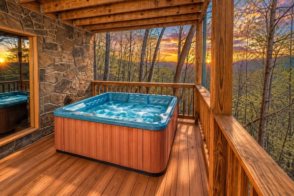 A hot tub on a wooden deck with a stone wall and a view of trees and mountains.