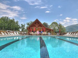 A swimming pool with lounge chairs and a wooden pavilion with umbrellas.