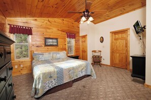 A wooden-paneled bedroom with a bed, dresser, and a ceiling fan.