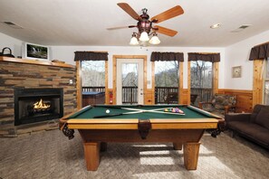 Un cuarto acogedor con mesa de billar, chimenea y vistas al exterior.