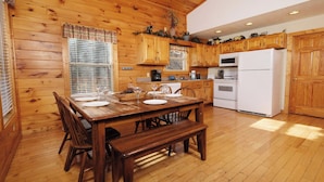 Un intérieur en bois avec une table à manger pour quatre personnes, des meubles de rangement en bois, un réfrigérateur blanc et une cuisinière.