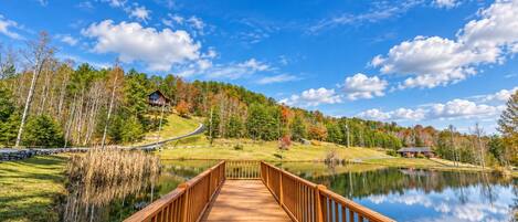 A wooden bridge leading to a house by a lake with a clear sky.