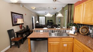 Una cocina con encimeras de granito, armarios de madera, lavavajillas y un comedor con mesa y sillas.