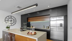 A modern kitchen with a central island, stainless steel appliances, and a large wall clock. - Penthouse in the City (Christchurch)