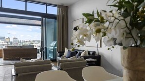 A modern living room with a glass door leading to a balcony, a sofa set, and a potted orchid. - Penthouse in the City (Christchurch)