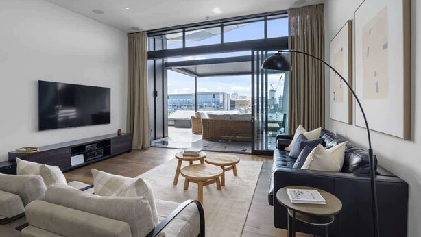 A modern living room with a flat-screen TV, leather sofa, and a large window offering a city view. - Penthouse in the City (Christchurch)