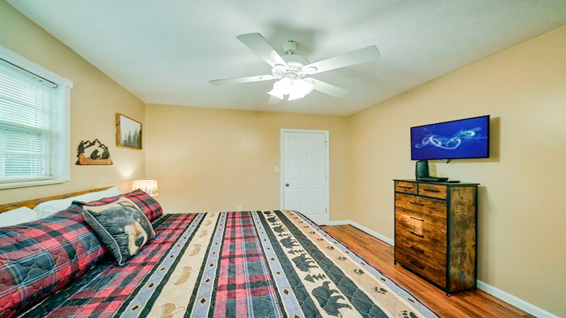 A bedroom with a bed, a ceiling fan, a television, and a dresser.