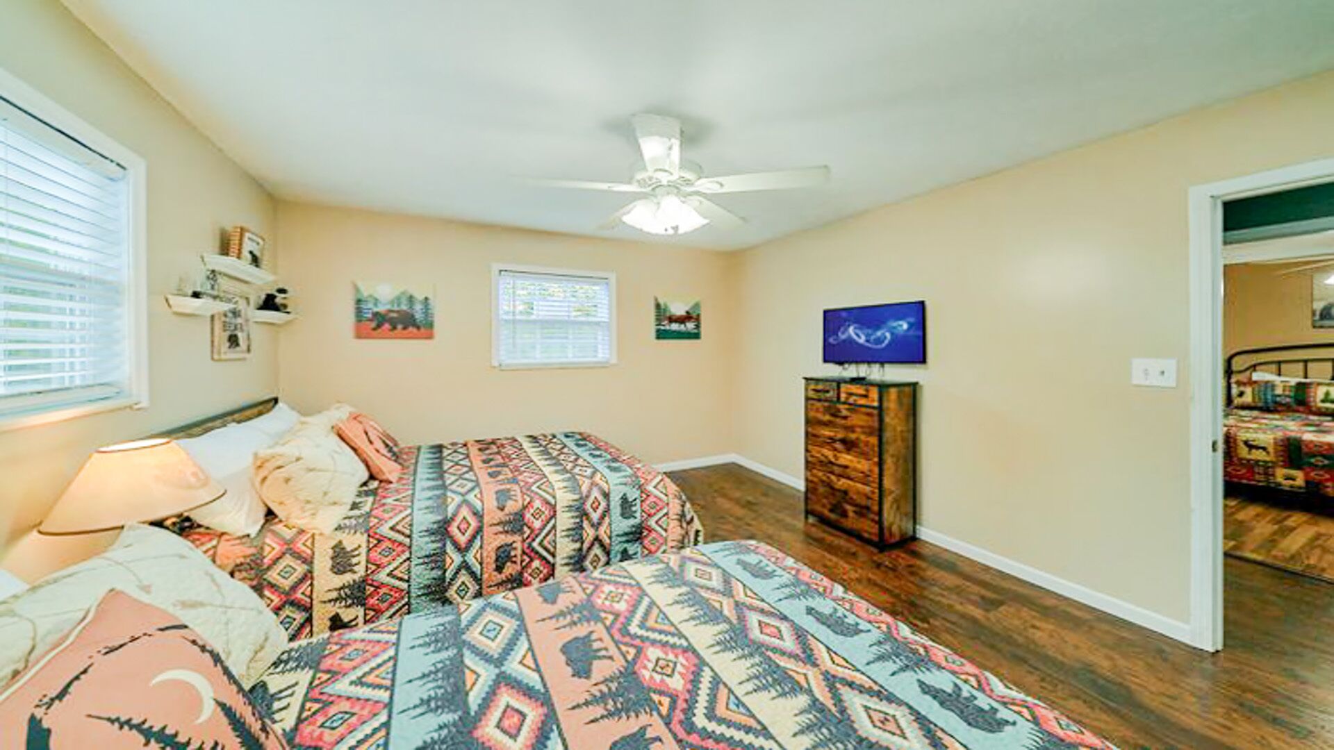 A bedroom with two beds, a ceiling fan, a TV, and a wooden dresser.