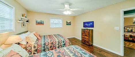 A bedroom with two beds, a ceiling fan, a TV, and a wooden dresser.